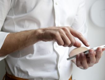 un homme en chemise blanche en train de consulter sur son téléphone portable l'application WaryMe PTI-DATI