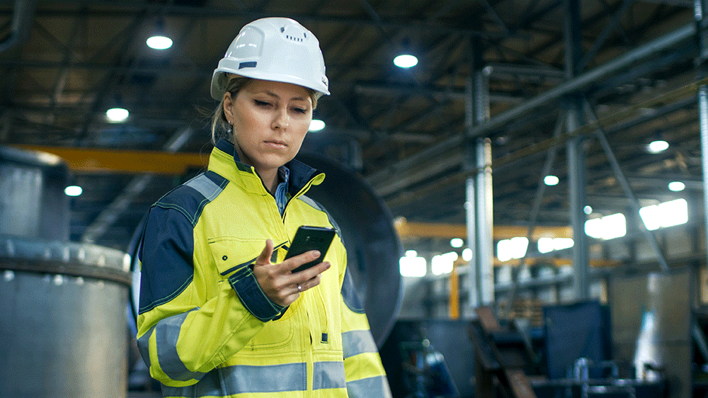 femme dans une usine regardant son téléphone sur lequel elle reçoit une alerte de détresse